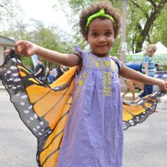 Young girl proudly displays butterfly wings at Earth Day fair.