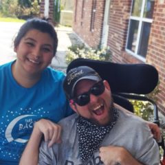 A helper poses with a man in wheelchair, both are smiling