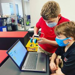 Two school-age boys using computer to program robot