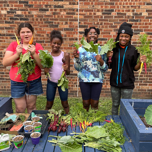 Four smiling kids hold up fresh produce from their community garden