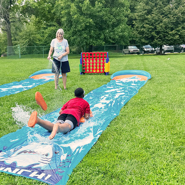 Boy plays on slip-n-slide on green lawn in summer