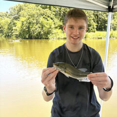 Young man standing by lake and holding up a fish